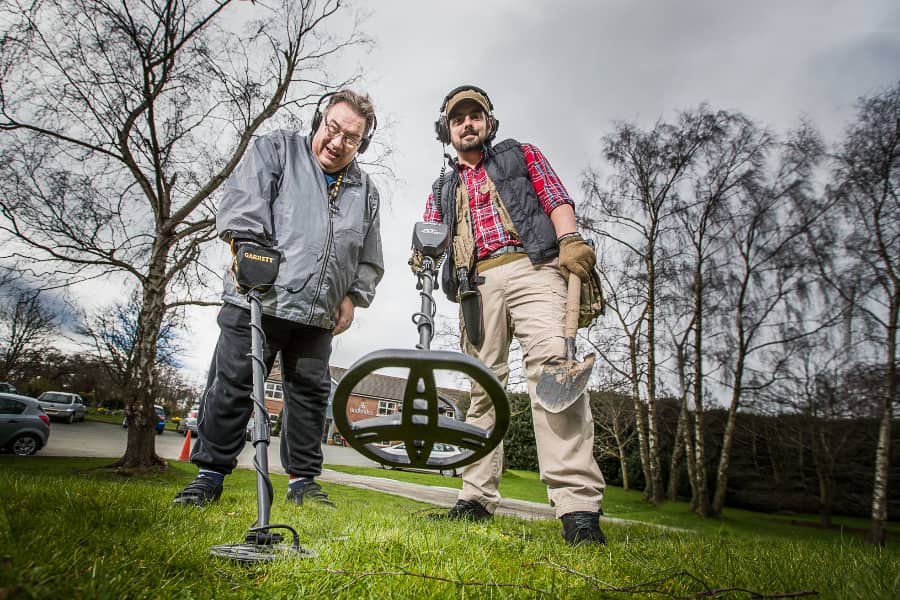 دو مرد در حال استفاده از فلزیاب روی چمن؛ مرتبط با نگهداری فلزیاب